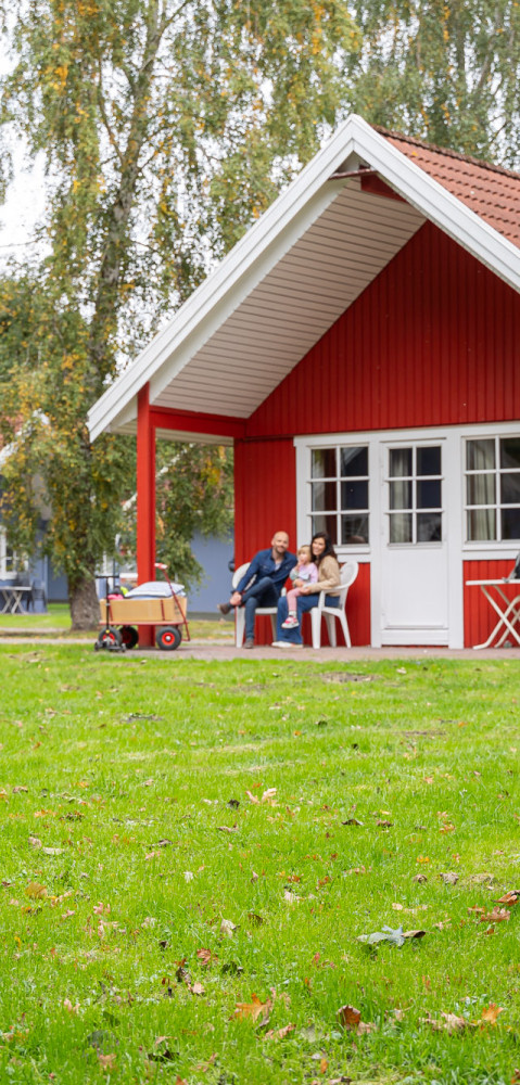 Ein Mädchen und ein Junge spielen Badminton im Vordergrund, im Hintergrund Familie vor einer roten Hütte im Campingplatz Baltic Freizeit in Markgrafenheide.