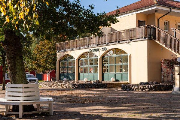 Baltic-SPA-Gebäude auf einem Campingplatz, flankiert von Bäumen mit herbstlichen Blättern und einer Bank im Vordergrund.