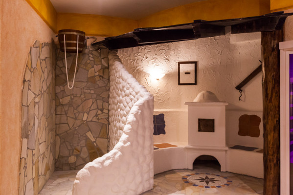 Detailansicht eines Entspannungsbereichs im 'Baltic Spa' des Campingplatzes mit Steinmauern, weißem Ornamentputz und traditionellem Ofen.