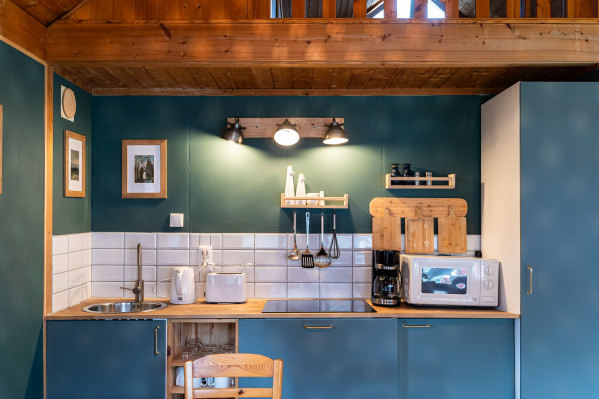 Innenansicht einer Küche mit blauen Schränken, weißen Kacheln und Holzakzenten, ausgestattet mit modernen Küchengeräten.