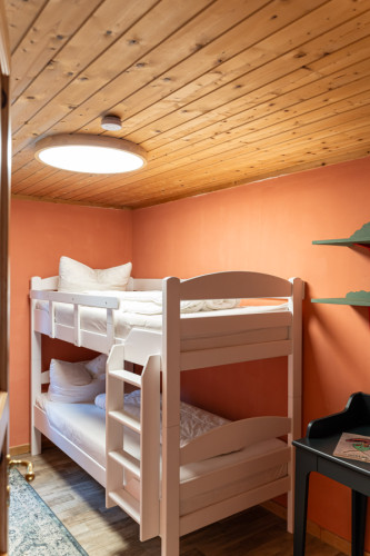 Kinderzimmer mit weißem Etagenbett, orangefarbener Wand und Holzdecke im Campingplatz Baltic Freizeit Markgrafenheide.