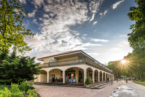 Gebäude mit Pool-Bereich, Restaurant und Wellness-Bereich auf dem Campingplatz von Baltic Freizeit in Markgrafenheide bei Sonnenuntergang mit Besuchern und umgebenden Bäumen.