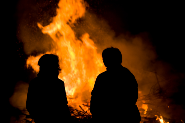 Zwei Personen im Schatten vor großem Feuer