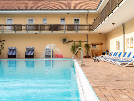 Schwimmbad mit Liegestühlen und Brunnen am Campingplatz, umgeben von Gebäuden.