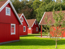 Rote Holzhäuser umgeben von grünen Bäumen und Wiese auf dem Campingplatz Baltic Freizeit in Markgrafenheide.