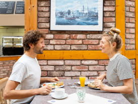Pärchen sitzt sich lächelnd gegenüber und frühstückt im Restaurant auf dem Campingplatz.