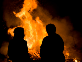 Zwei Personen im Schatten vor großem Feuer