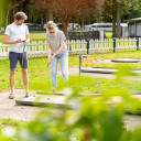 Junges Paar spielt Minigolf auf dem Gelände von Baltic Freizeit, umgeben von grüner Natur und Wohnmobilen."