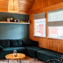 Gemütliches Wohnzimmer mit grünem Samtsofa, hölzernem Couchtisch und Bücherregal, umgeben von Holzwänden und Fenstern.