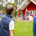 Mädchen spielt Badminton im Vordergrund, im Hintergrund Familie vor einer roten Hütte im Campingplatz Baltic Freizeit in Markgrafenheide.