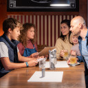 Familie mit drei Kindern in gemütlicher Ecke vom Restaurant wählen Speisen von der Karte aus.